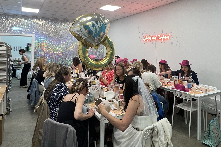 Group wearing cowboy hats pottery painting, with bride wearing veil in foreground and ring-shaped balloon